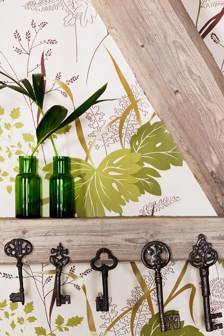 Collection of vintage keys hung from half-timber beams and green glass vases against leaf-patterned wallpaper