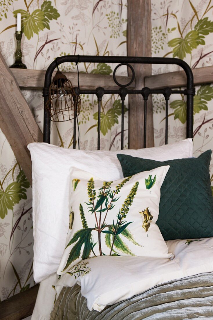 Green and white scatter cushion on black metal bed against half-timbered wall with wallpapered panels with botanical pattern