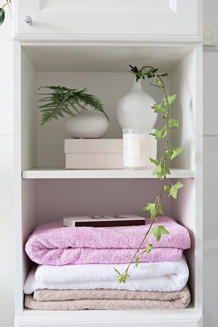Stacked towels and foliage in white vases on bathroom shelves
