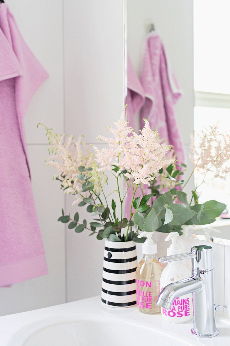 Vase of flowers on sink and soap dispensers with pink lettering