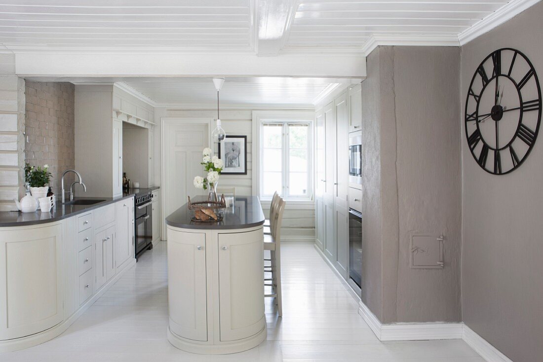 Open-plan, designer kitchen with free-standing counter and large clock on wall painted warm grey