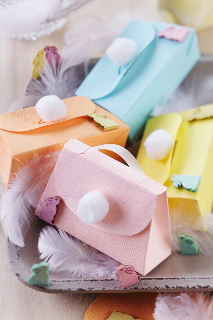 Colourful, spring-themes paper gift boxes shaped like handbags with handles and pompoms
