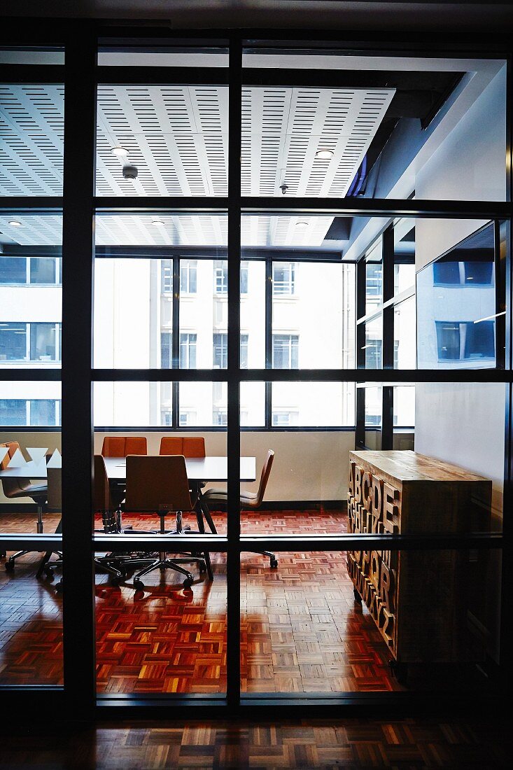 Blick durch raumhohes Fensterelement mit Sprossen in Besprechungsraum, im Hintergrund sonnenbeschienene Hausfassaden