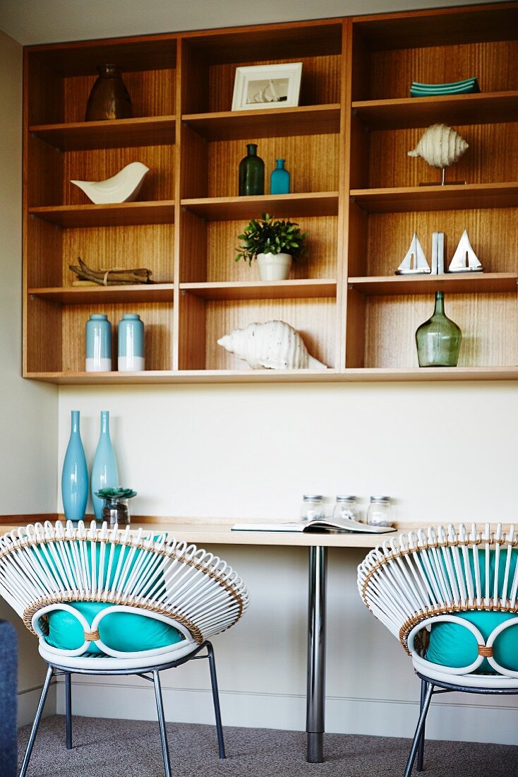 White basket chairs with turquoise cushions at worksurface below shelving with wooden back wall