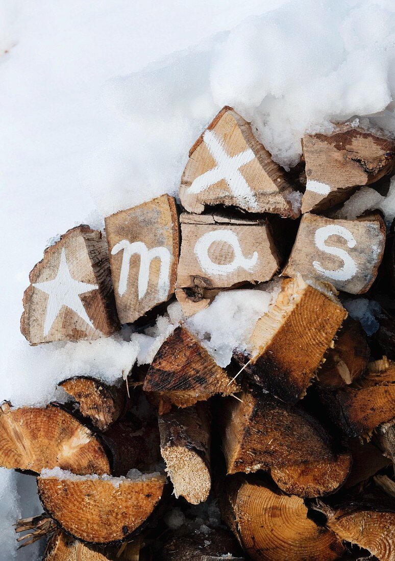 Christmas greeting painted on stacked firewood with white acrylic paint surrounded by snow
