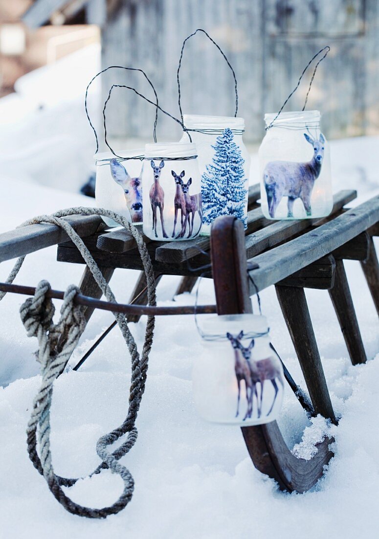 Selbstgebastelte Windlichter aus Joghurtgläsern mit Rehmotiven auf Schlitten im Schnee