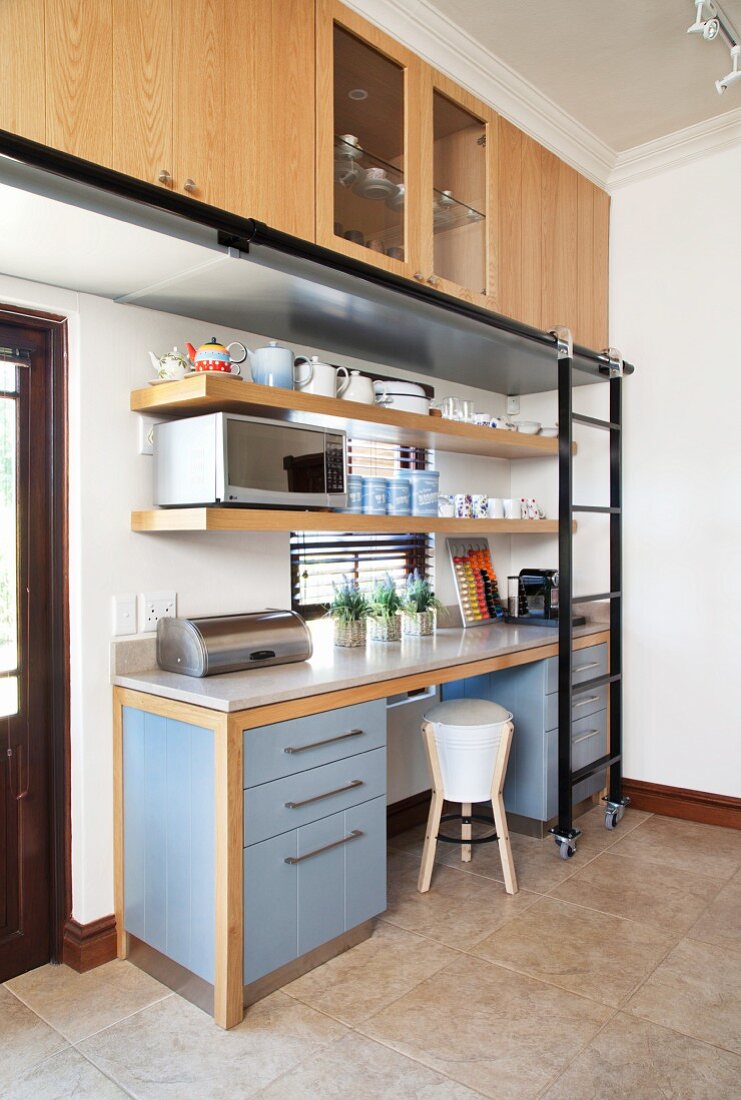 Küchenzeile mit blauen Unterschränken unter Stein Arbeitsplatte, darüber Hängeschränke mit montierter Schiene und verschiebbarer Leiter