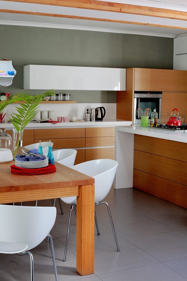 White shell chairs at solid wooden table in kitchen; drawers in wooden-fronted base units below white worksurface