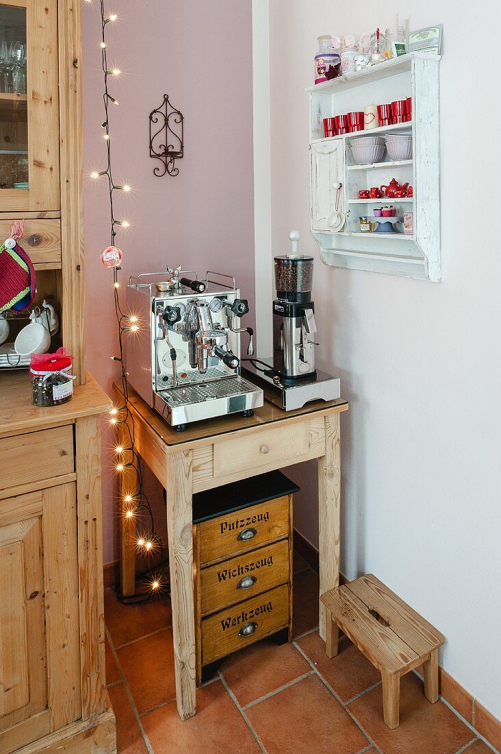 Rustikaler Beistelltisch mit Kafeemühle und Espressomaschine in Küchenecke neben weisses Gewürzregal an Wand