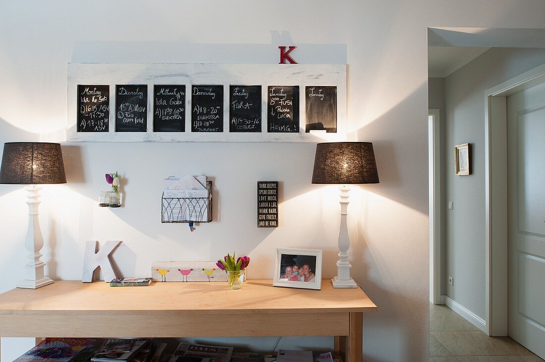 Modern wooden table with two table lamps below framed blackboards on wall