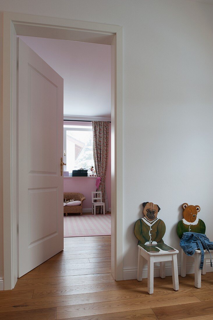 Children's chairs with carved, painted, animal backrests next to open door leading to child's bedroom