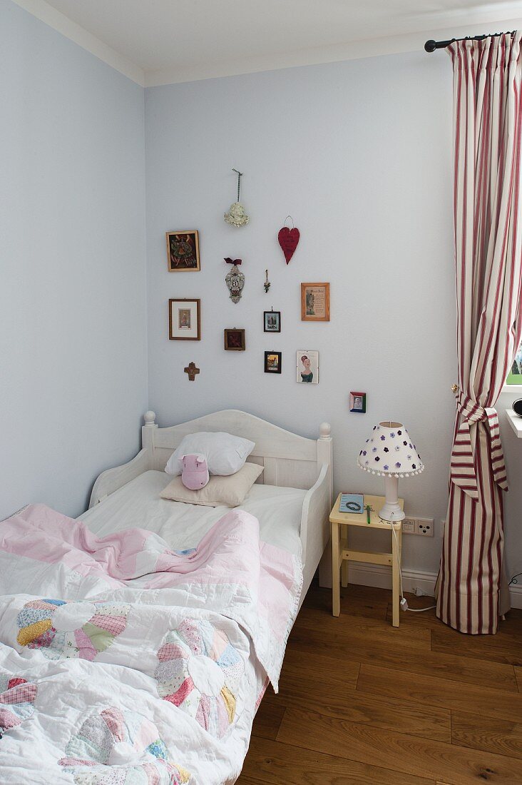 Child's bed with white wooden frame, bedside table and red and white striped curtains