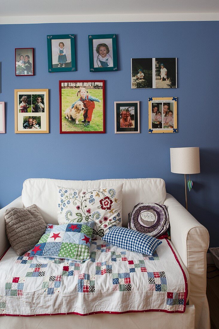 Patchworkdecke und Kissen auf ausziehbarem Sessel vor blau getönter Wand, mit aufgehängten Bildern