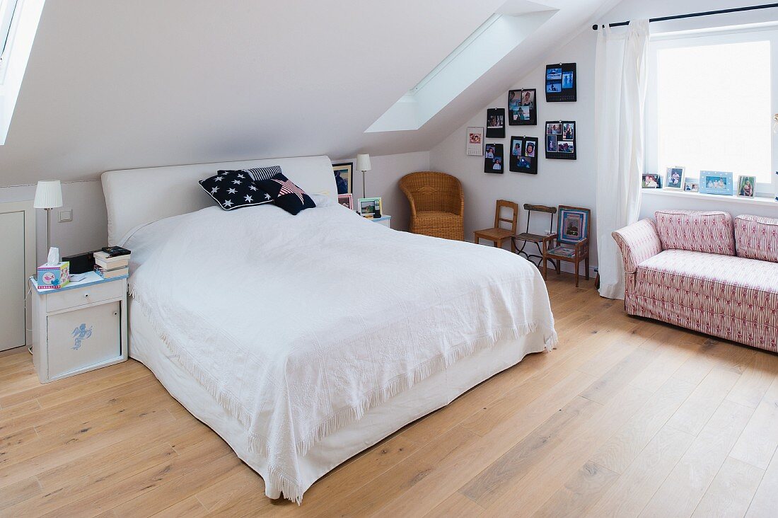 Doppelbett mit Kopfteil und weisser Decke und gemustertes Sofa im Dachzimmer