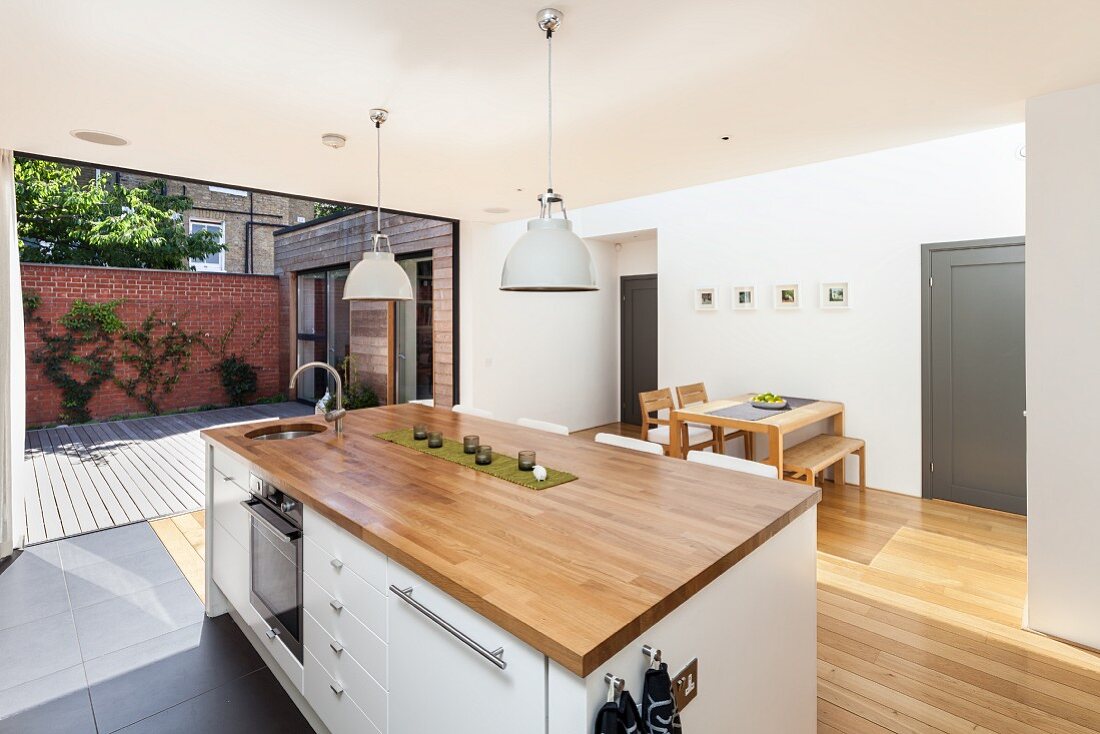 Kitchen island with wooden worksurface below retro pendant lamps; open folding doors leading to courtyard in background
