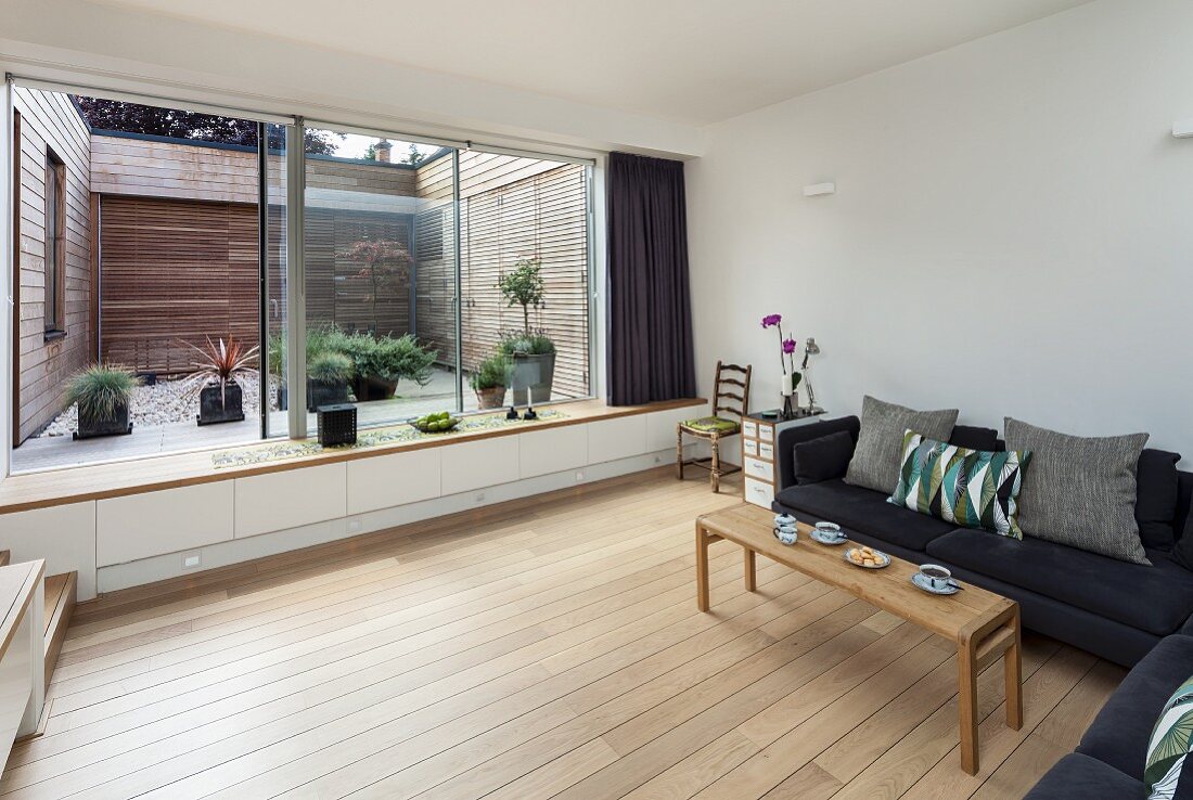 Wohnzimmer mit Sofa auf Dielenboden, Fensterfront mit eingebauter Bank und Blick in Innenhof