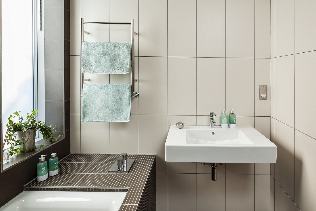 Waschbecken an Wand mit weissen, hochformatigen Fliesen , seitlich eingebaute Badewanne am Fenster im Designerbad