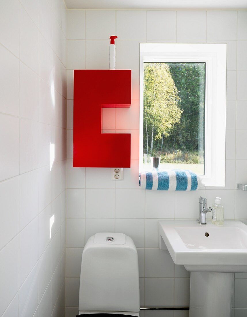 Red, wall-mounted cabinet next to window in white bathroom