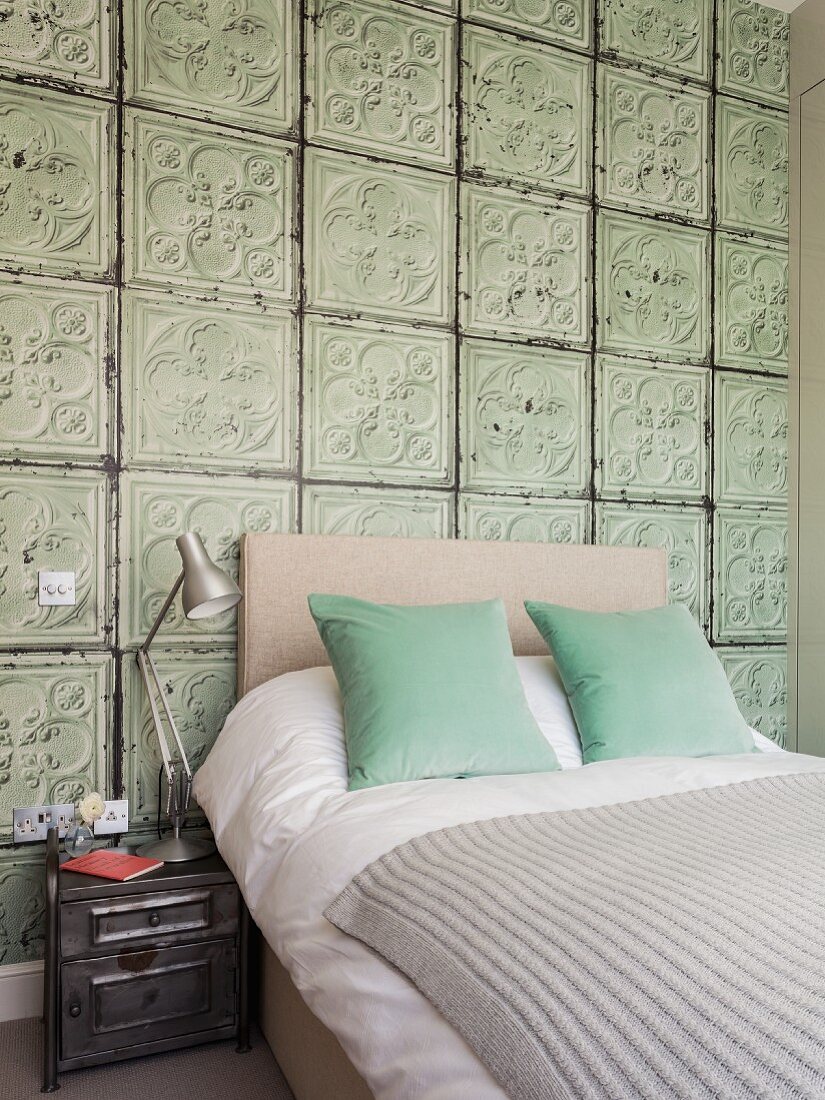 Double bed with headboard against wall covered in old 3D structured tiles in bedroom