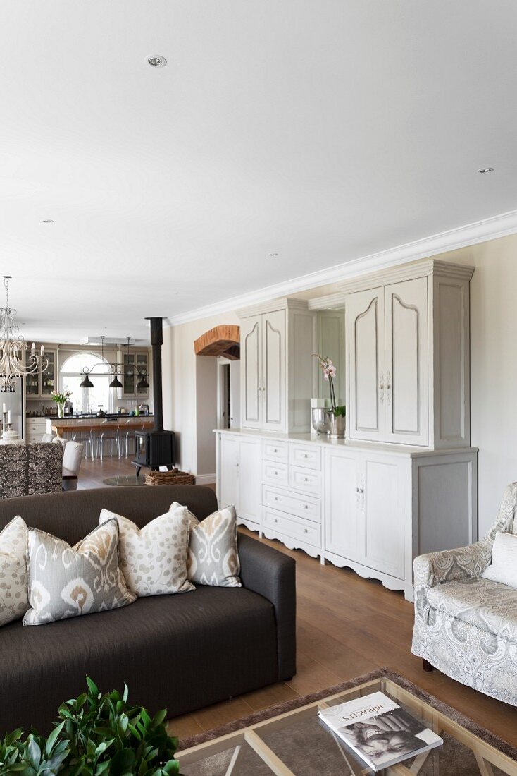White, elegant, country-house-style dresser between seating area and dining area in open-plan interior