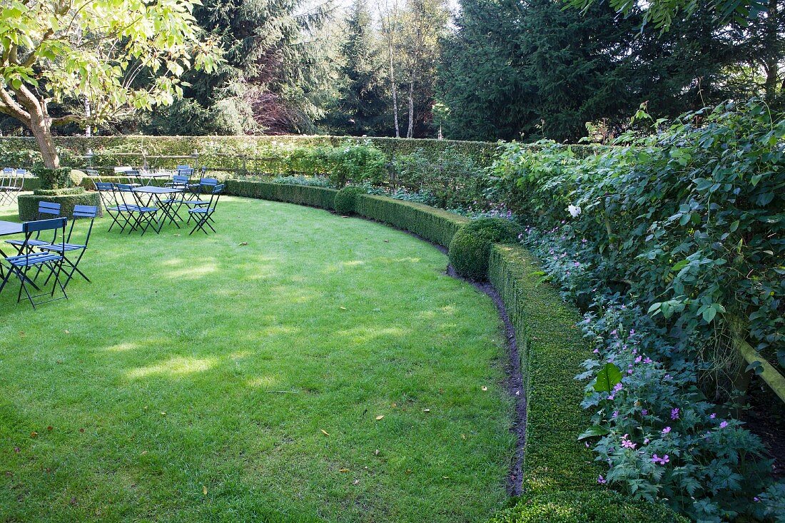 Lawn edged by curved hedge with garden tables and chairs in background