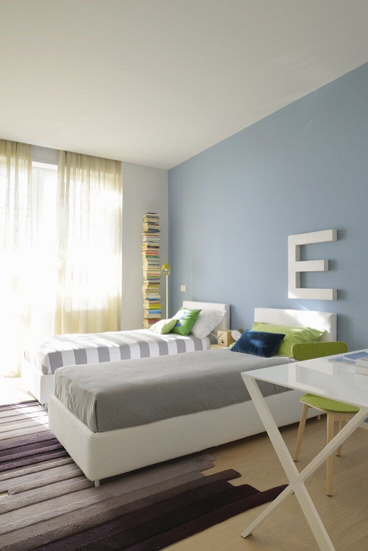 Twin beds with white frames and headboards against pastel blue wall in modern interior