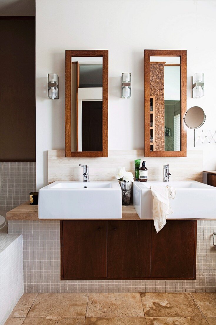 Twin sinks on masonry washstand with integrated cupboard below tall narrow mirrors on wall