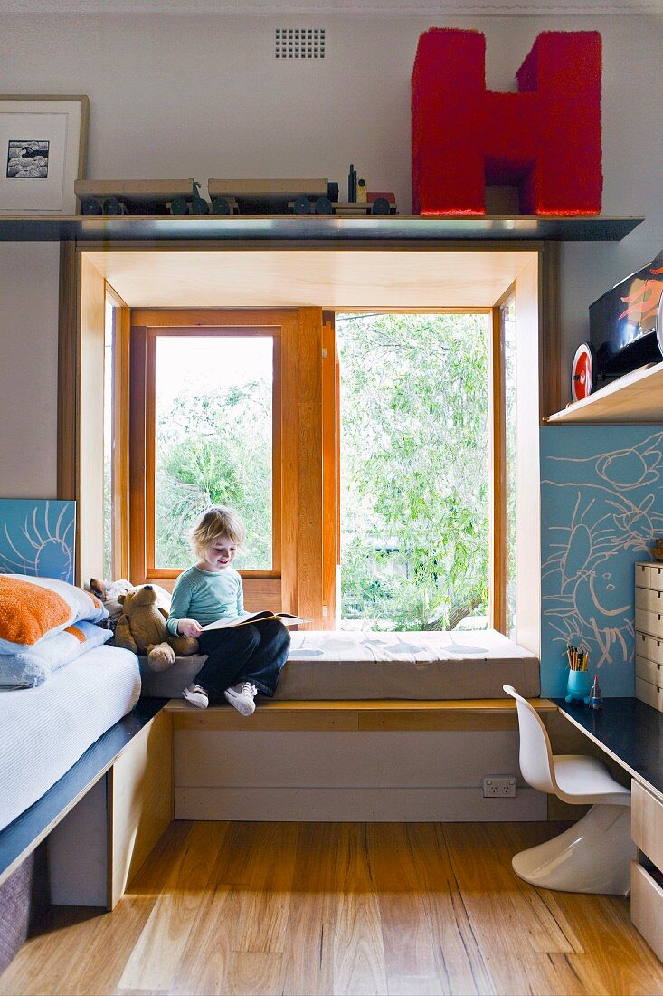 Kind in Fenstererker auf Sitzpolster, neben Bett, gegenüber Klassiker Kinderstuhl aus weißem Kunststoff