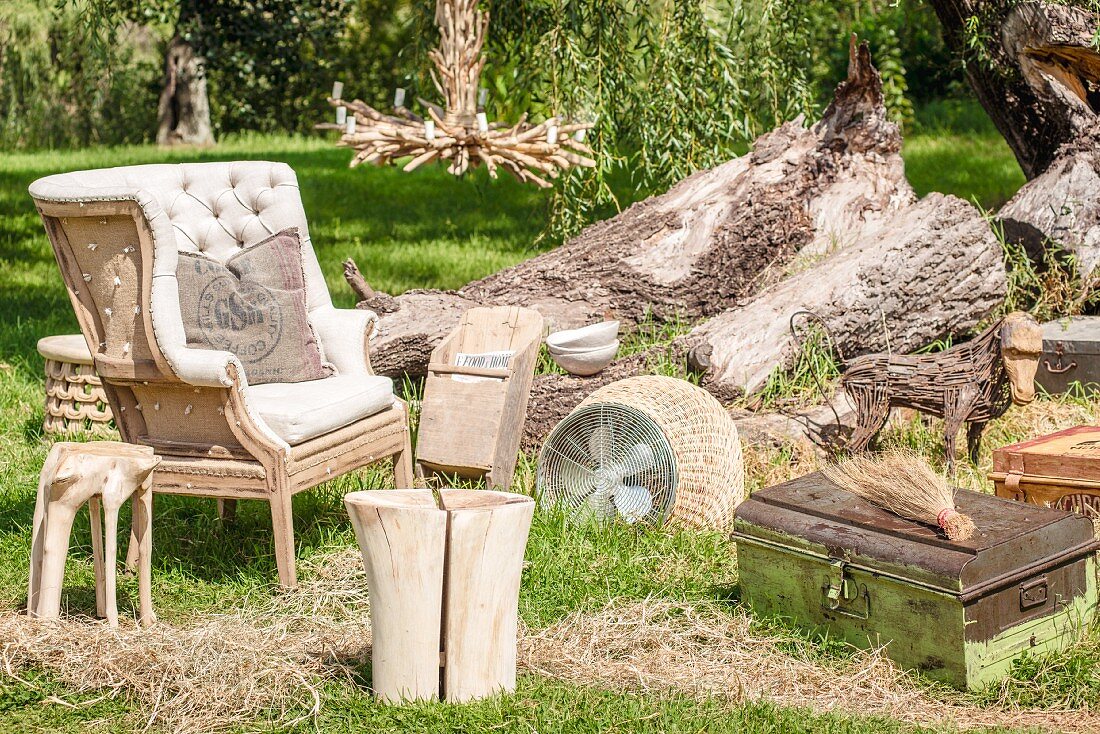 Small items of vintage furniture, armchair, tree stump stool and candlestick on summery lawn