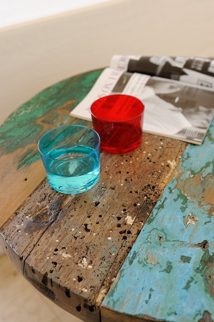 Farbige Trinkgläser auf rundem Vintage Tisch aus recyceltem Holz