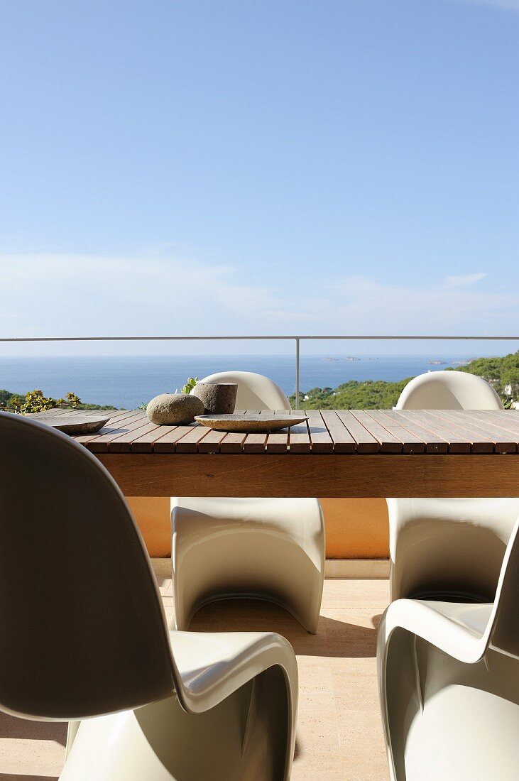 Holztisch und Pantonstühle auf sonniger Terrasse mit Meerblick