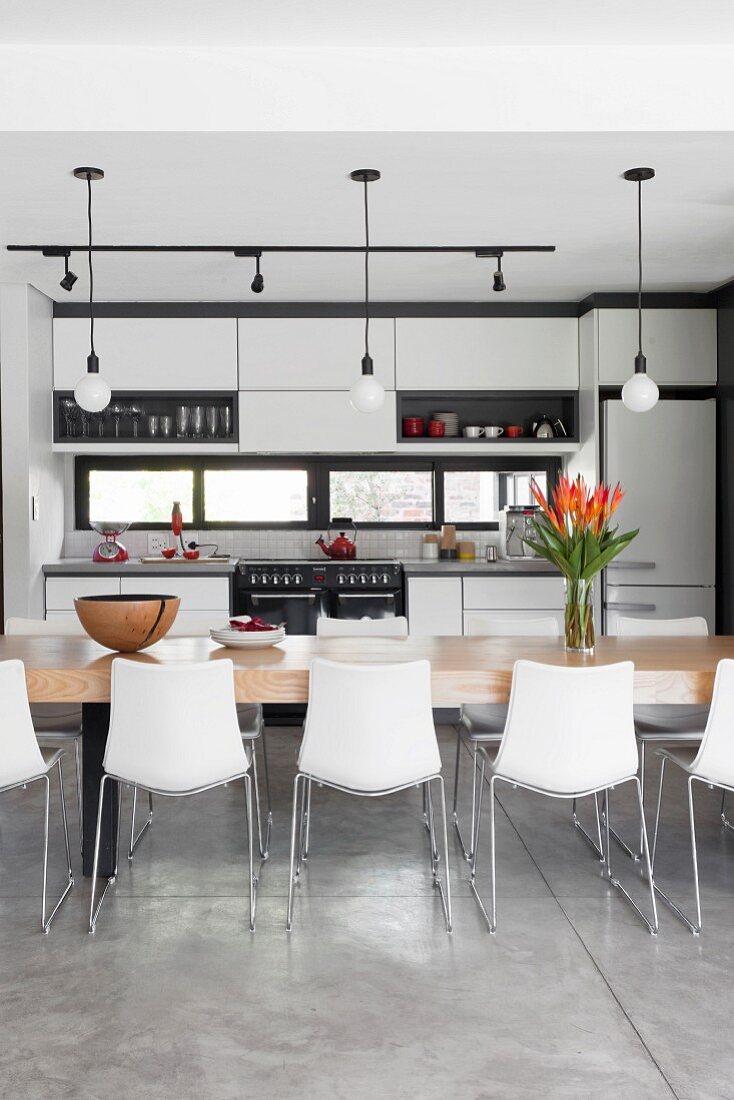 Open-plan kitchen with long table and shell chairs below simple pendant lamps