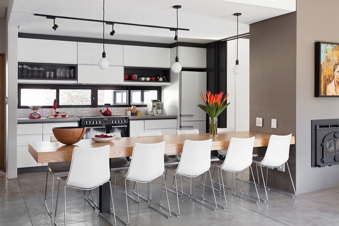 Dining table with 10 light shell chairs in front of modern, white fitted kitchen