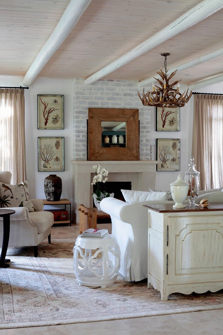 Interior with pale, country-style decor accentuated by varnished ceiling and whitewashed brick wall above fireplace
