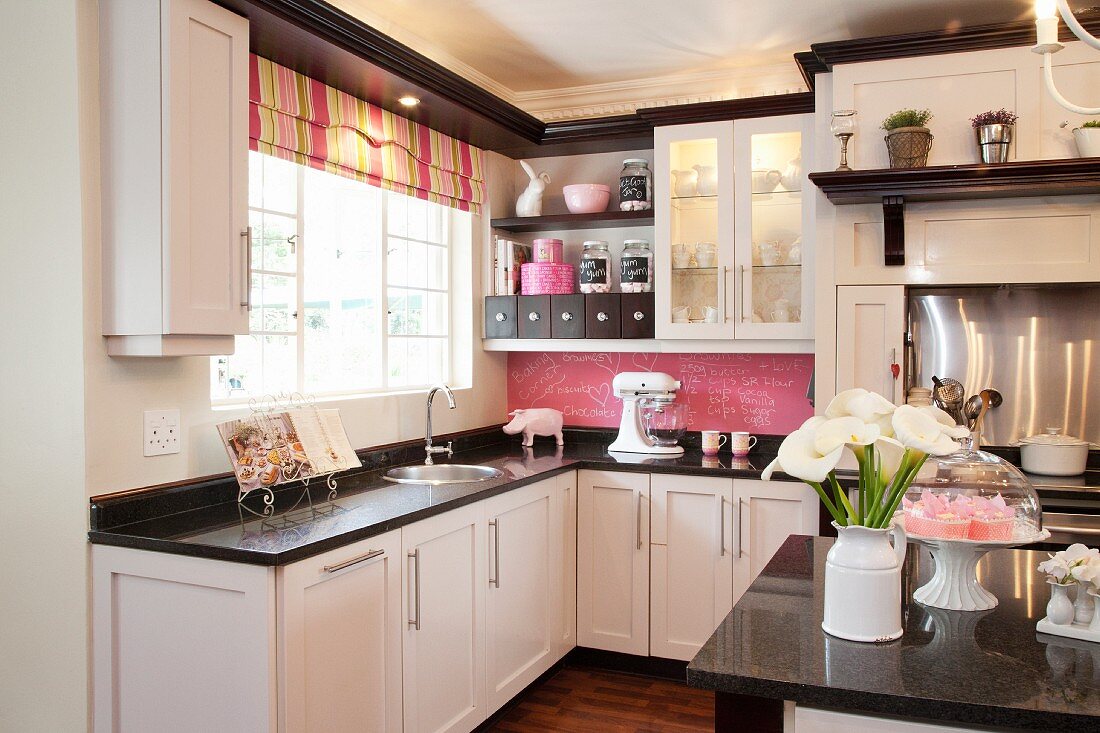 Schwarz-weiße Einbauküche mit gestreiftem Faltrollo und pinkfarbenem Spritzschutz als Kreidetafel