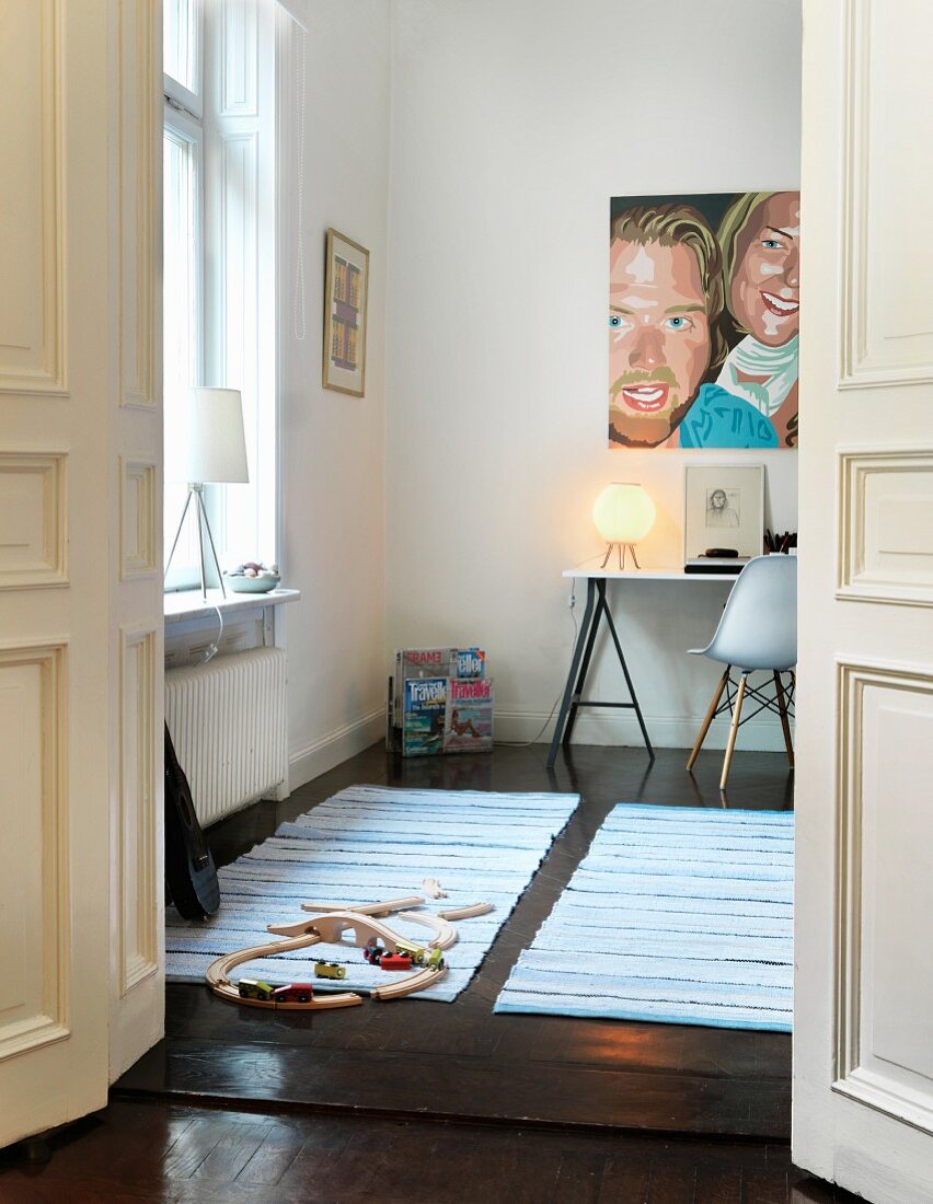 Open double doors leading to boy's room; train set on rug and painting on wall above desk