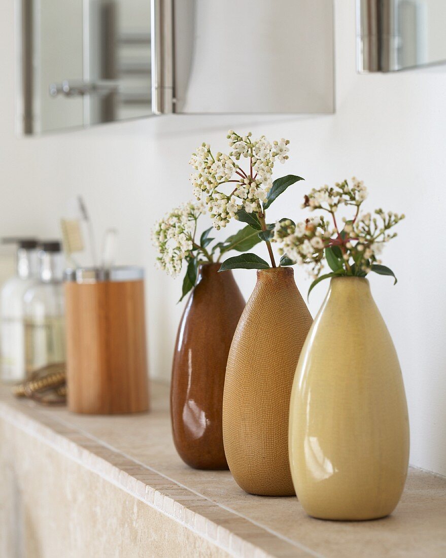 Drei nebeneinander stehende Vasen aus Keramik in verschiedenen Brauntönen mit Blütenzweig