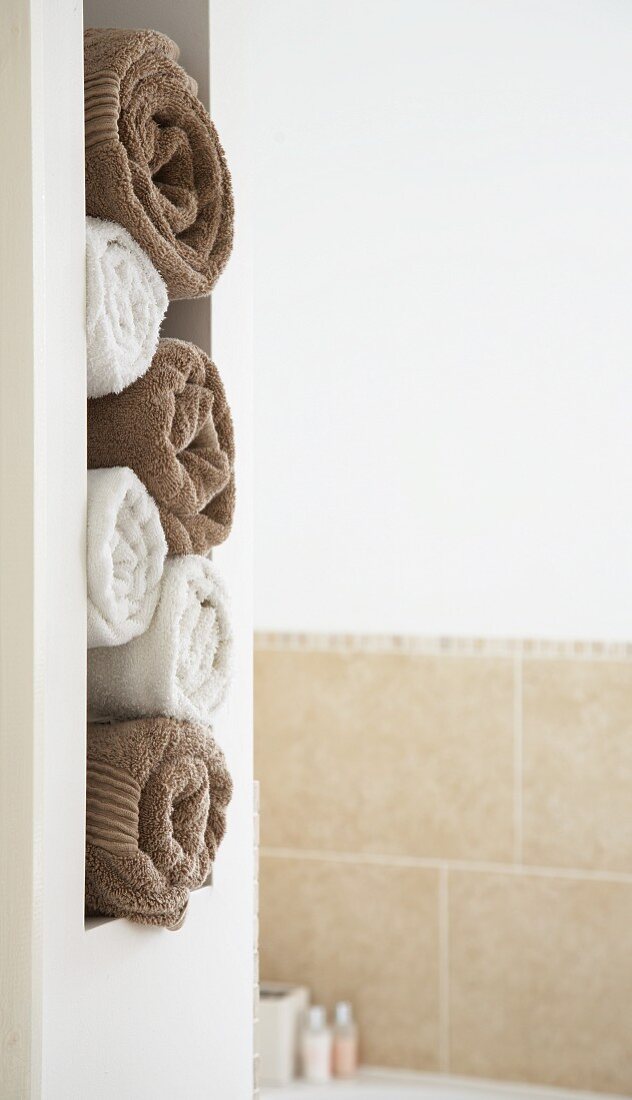 Gerollte Handtücher in Weiß und Braun in gemauerter Regalöffnung eines Bades