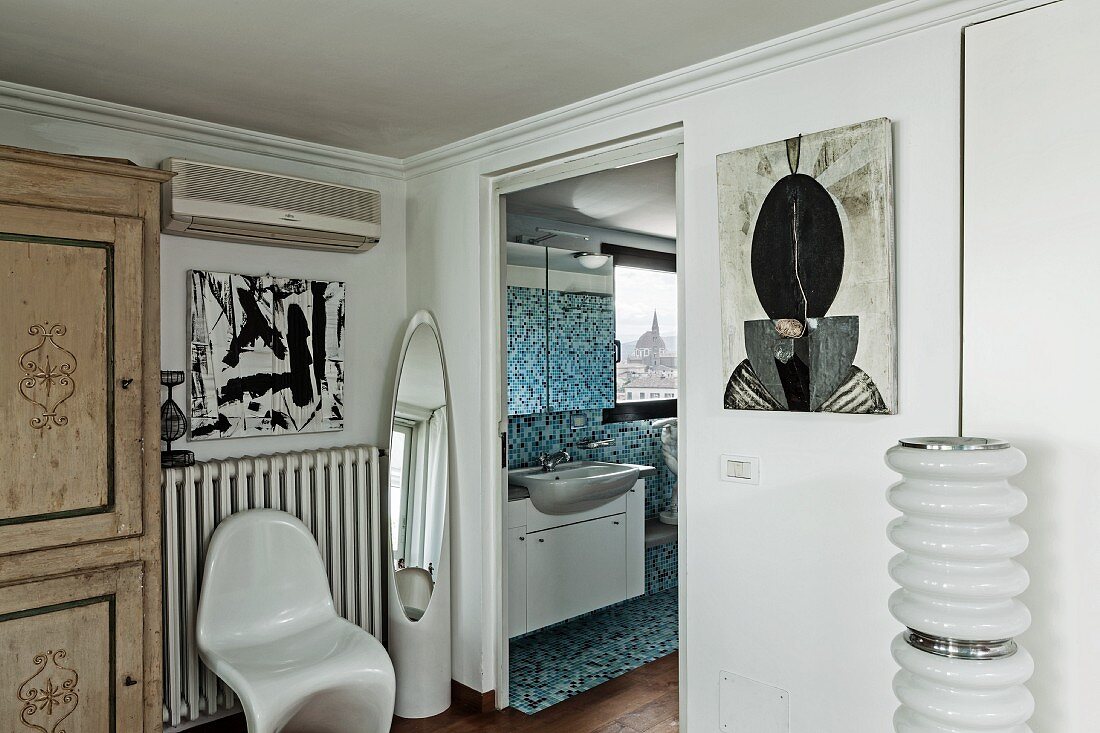 Wohnraumecke mit Klassikerstuhl aus weißem Kunststoff neben offener Tür und Blick ins Bad