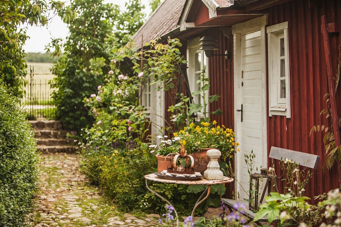 Schlichtes Holzhaus, davor Gartentisch mit Blumentöpfen
