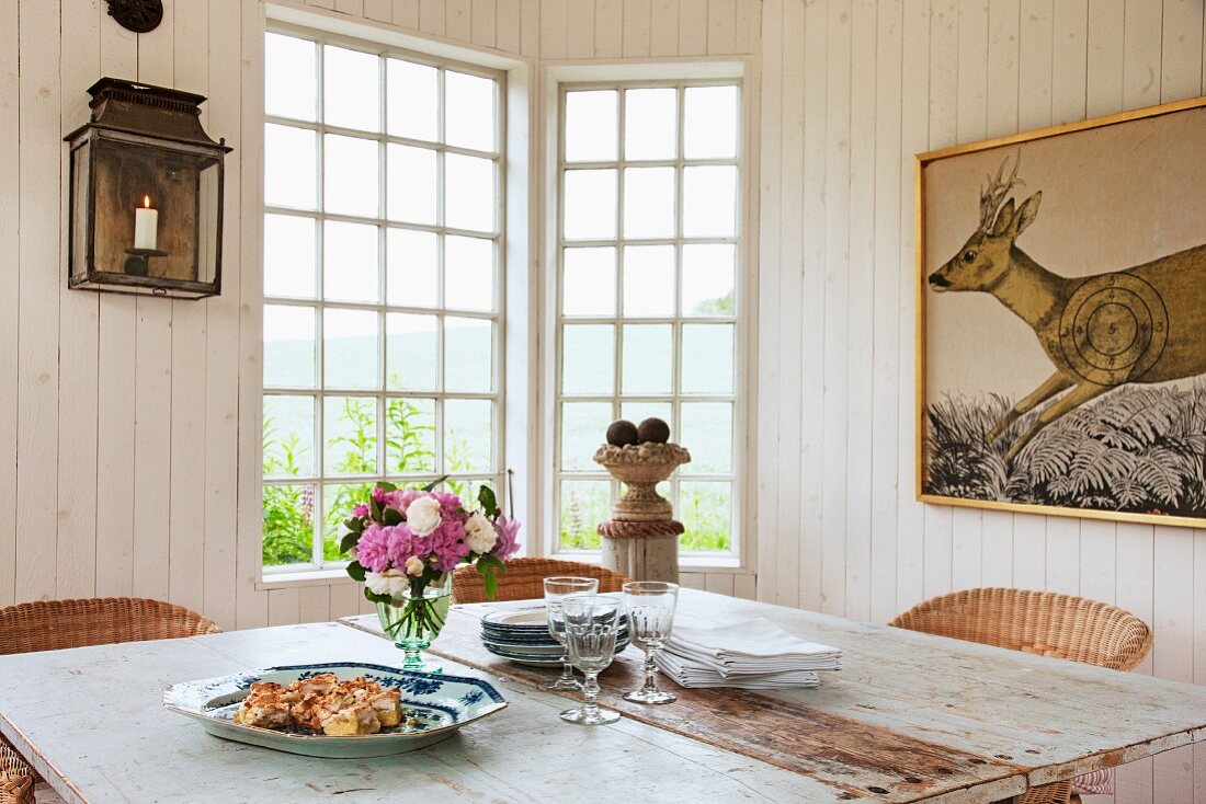 Rustikaler Holztisch in Polygoner Gartenpavillon mit Sprossenfenster, Bild mit Elchmotiv an Holzwand
