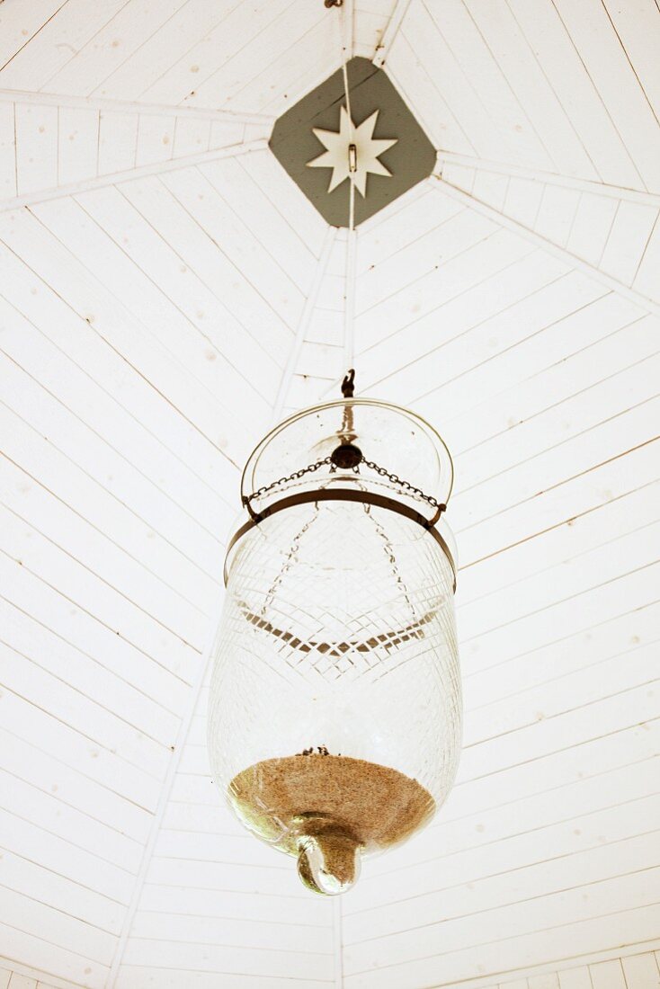 Pendant lamp with glass lampshade hanging from white-painted wooden ceiling