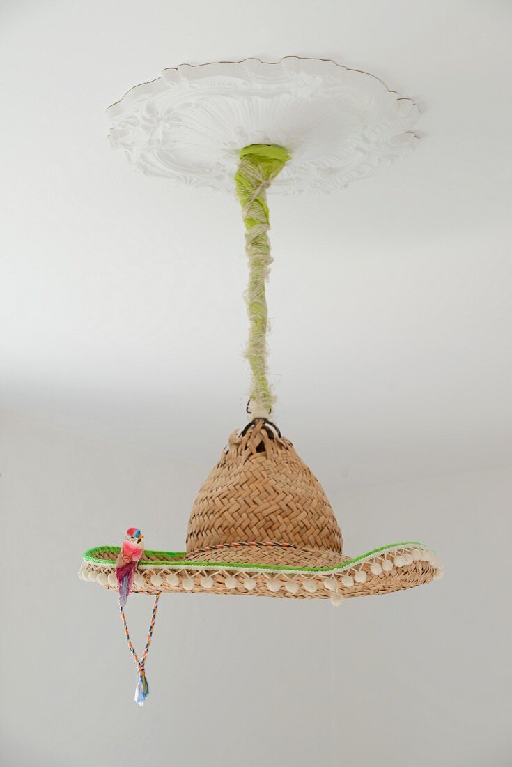 Deckenleuchte mit improvisiertem Lampenschirm aus Sombrero Strohhut und Deko Vögelchen, an weisser Stuckdecke