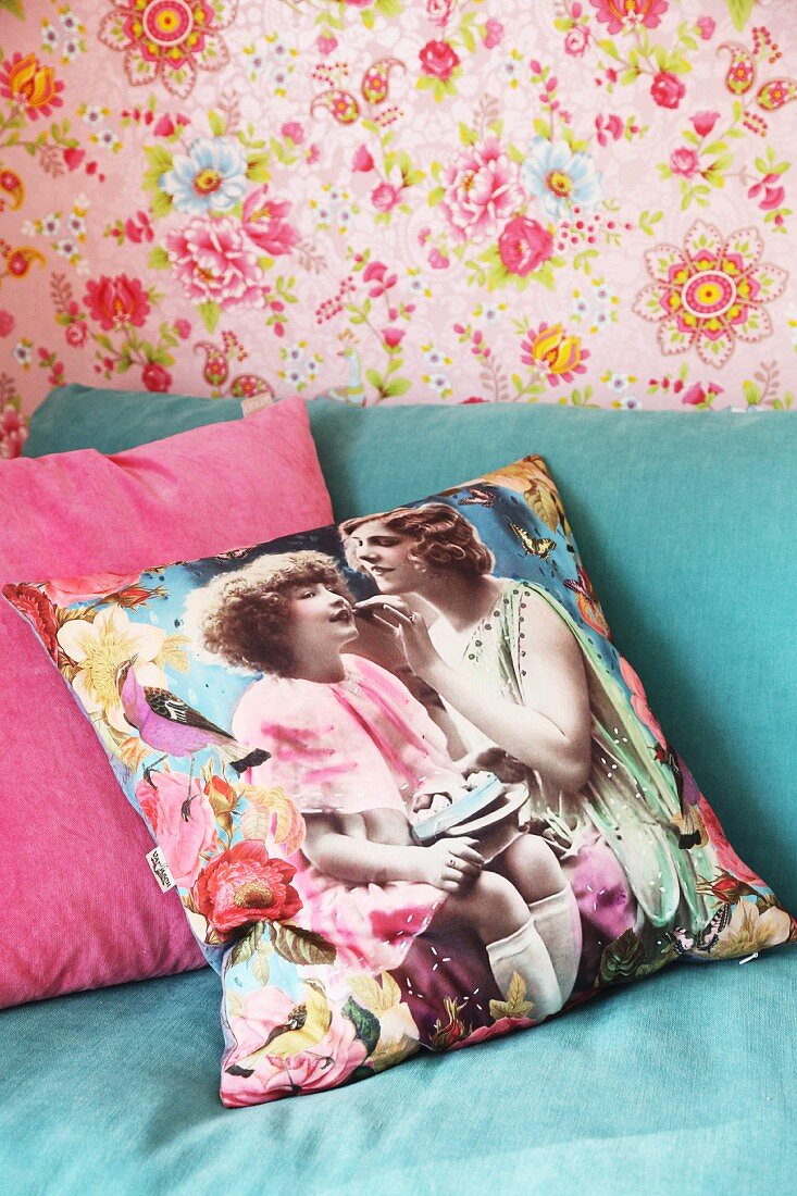 Kissenbezug mit nostalgischem Fotodruck, auf türkisfarbenem Sofa vor rosafarbener Blumentapete