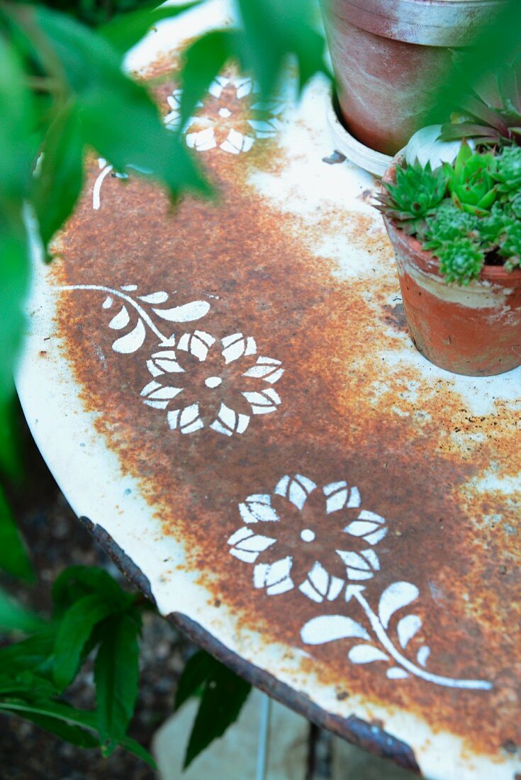 Rostiger alter Gartentisch mit schabloniertem Blumendekor, darauf Hauswurz im Tontopf