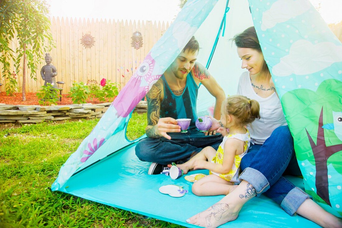 Junges Paar spielt mit Tochter Teatime in einem Zelt im Garten