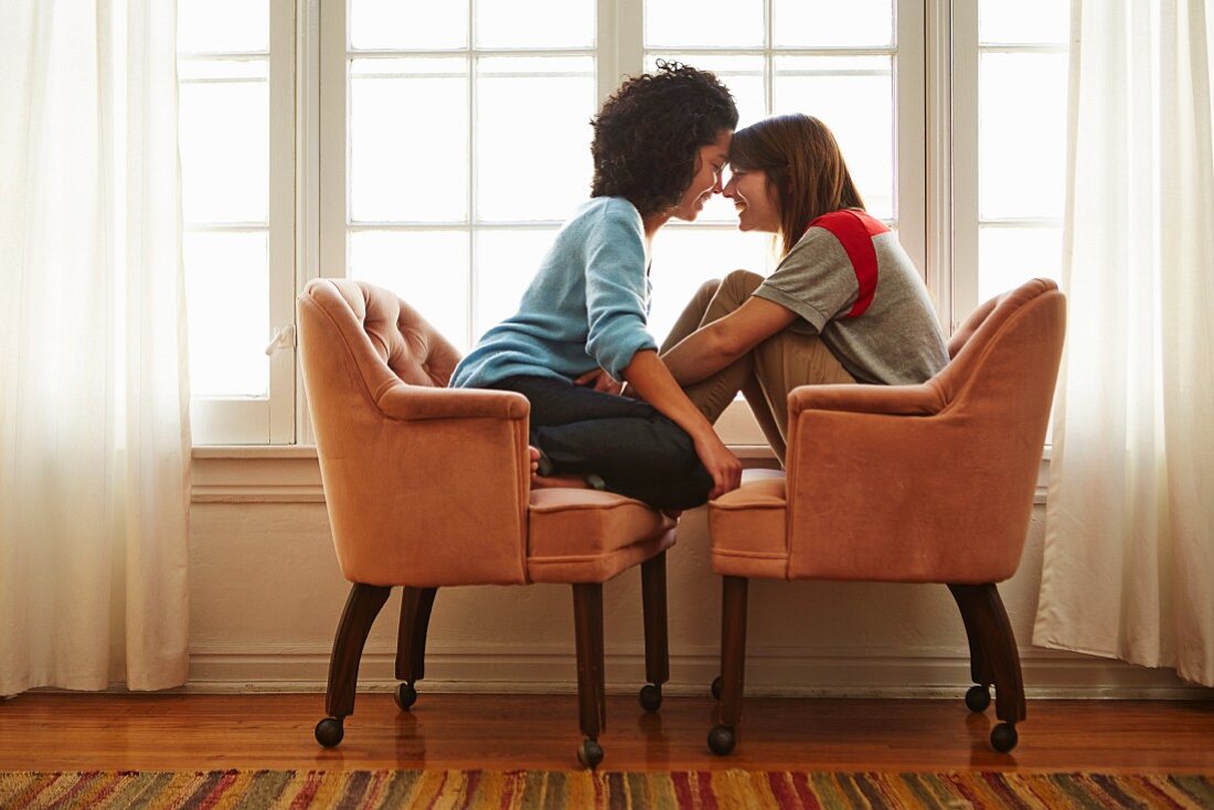 Young female couple sitting head to head in two armchairs pushed together