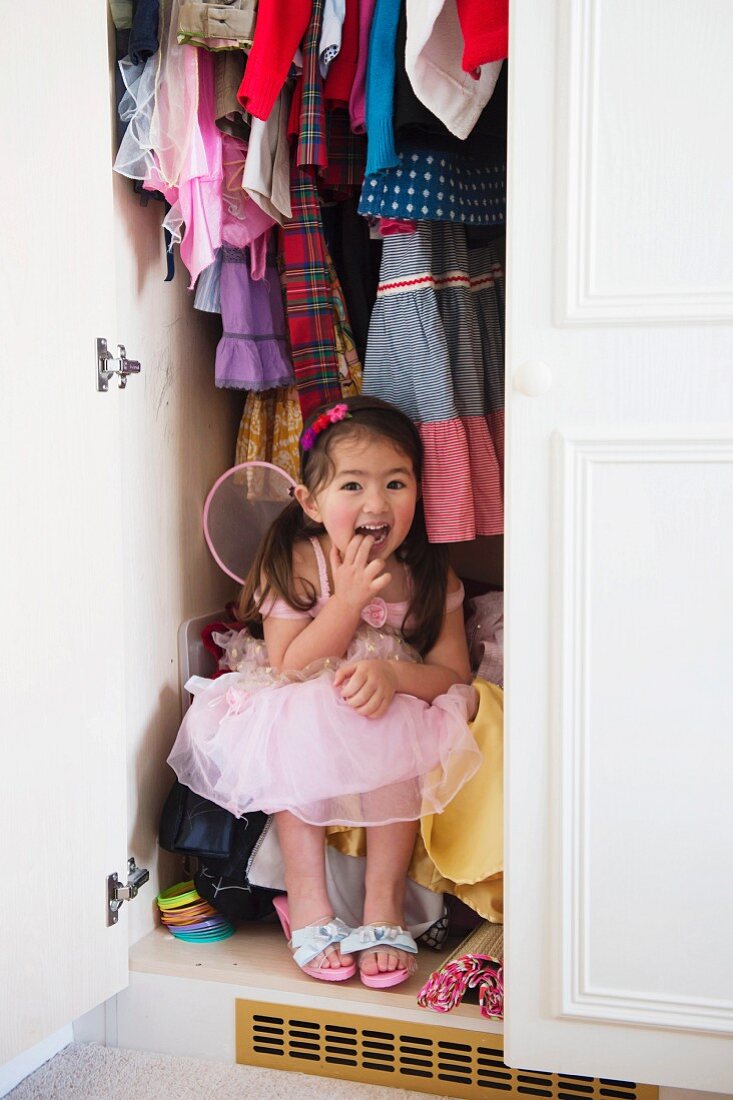 Mädchen in Prinzessin-Kostüm versteckt sich im Kleiderschrank