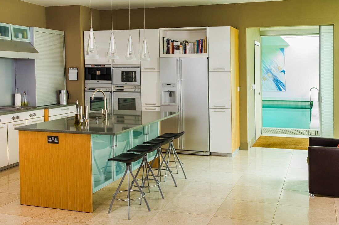 Kücheninsel mit Arbeitsplatte aus hellgrauem, poliertem Stein, davor Barhocker in offener Einbauküche mit Zugang zum Pool