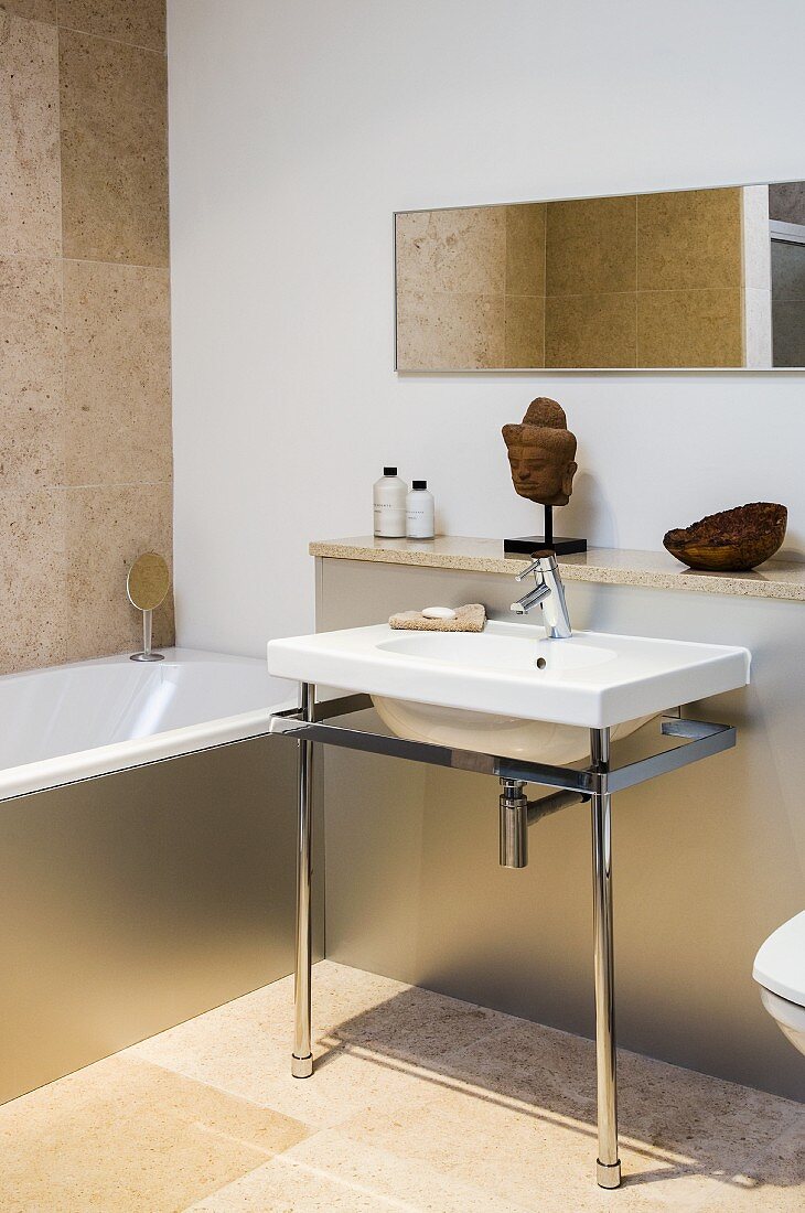 Minimalistischer Waschtisch mit Metallgestell, Vormauerung und Badewanne mit Metallverkleidung in Badezimmer mit sandfarbener Kalksteinboden